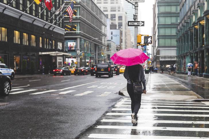 A person with a pink umbrella in a city sidewalk.